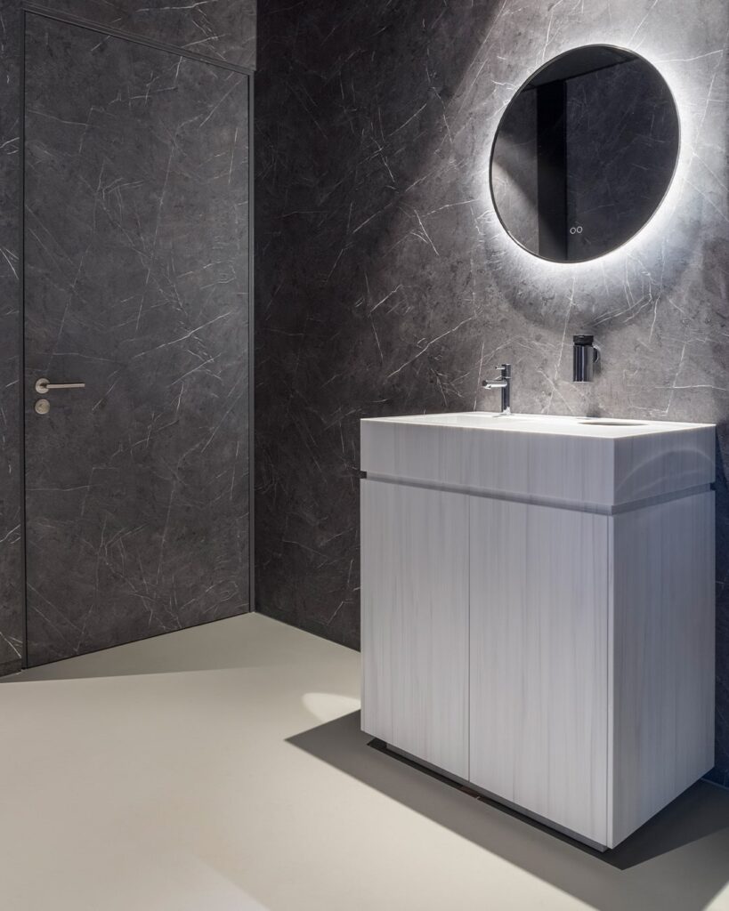 Toilet in de showroom van DecoLegno waarbij de muren zijn uitgevoerd in de FC19 Talco van Cleaf, een donkergrijze marmerlook met ultra matte finish, en het wastafelmeubel in de DM5015 Luna van Durasein, met een vloeiend lijnenspel in een serene, witte kleurmelange.