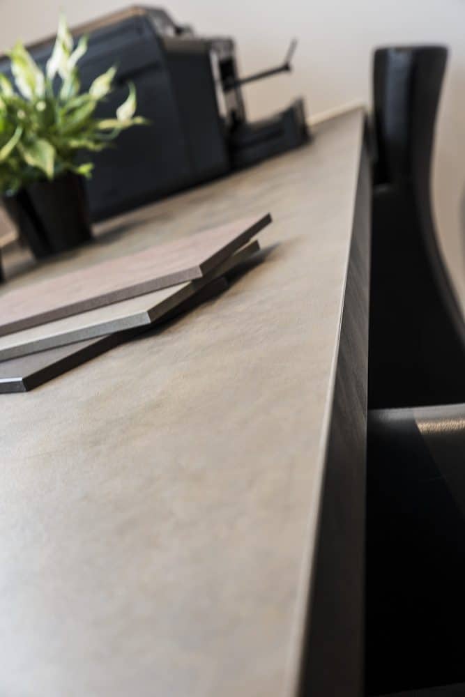 Close up van een werkblad dat is gemaakt van decoratief plaatmateriaal van Cleaf. De FB47 Ares heeft een voelbare structuur in een warm grijze ondergrond, met donker gouden accenten