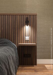 Een close up van een bed met een bed achterwand waarin houten latten zichtbaar zijn. De achterwand is gemaakt van decoratief plaatmateriaal, de LR28 Sable van Cleaf, met een warm hout decor.